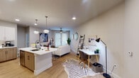 This single-floor residence is thoughtfully designed with a contemporary aesthetic and a functional open-concept layout. The kitchen serves as a central hub, featuring two-tone cabinetry that pairs white upper cabinets with light wood lower cabinets, white quartz countertops, a classic subway tile backsplash, and stainless steel appliances including a range, microwave, and dishwasher. A peninsula with seating extends into the living area, creating a seamless transition between cooking and entertaining spaces. Recessed lighting and pendant fixtures illuminate the kitchen effectively.

The open living area accommodates both a comfortable seating arrangement and a dedicated workspace. Light wood-style flooring runs throughout, adding warmth, while a ceiling fan provides additional comfort. French-style doors allow natural light to filter into the main living space.

A separate sitting nook features hardwood flooring, a round mirror, and curated décor, adding a refined touch to the layout. The bedroom offers plush carpeting, dual windows with blinds that invite natural light, a ceiling fan, and direct access to a spacious walk-in closet with built-in shelving and hanging storage.

The bathroom is finished with taupe subway tile surrounding a full soaking tub and shower, complemented by a white quartz vanity, wood-toned cabinetry, and a large mirror.