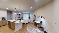 This single-floor residence is thoughtfully designed with a contemporary aesthetic and a functional open-concept layout. The kitchen serves as a central hub, featuring two-tone cabinetry that pairs white upper cabinets with light wood lower cabinets, white quartz countertops, a classic subway tile backsplash, and stainless steel appliances including a range, microwave, and dishwasher. A peninsula with seating extends into the living area, creating a seamless transition between cooking and entertaining spaces. Recessed lighting and pendant fixtures illuminate the kitchen effectively.

The open living area accommodates both a comfortable seating arrangement and a dedicated workspace. Light wood-style flooring runs throughout, adding warmth, while a ceiling fan provides additional comfort. French-style doors allow natural light to filter into the main living space.

A separate sitting nook features hardwood flooring, a round mirror, and curated décor, adding a refined touch to the layout. The bedroom offers plush carpeting, dual windows with blinds that invite natural light, a ceiling fan, and direct access to a spacious walk-in closet with built-in shelving and hanging storage.

The bathroom is finished with taupe subway tile surrounding a full soaking tub and shower, complemented by a white quartz vanity, wood-toned cabinetry, and a large mirror.