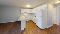 This single-floor unit features a cohesive design highlighted by warm-toned wood-look flooring that flows consistently throughout every room, creating a unified and inviting atmosphere. The living area is comfortably sized and equipped with a ceiling fan with integrated lighting, neutral gray-toned walls, and a large sliding door fitted with vertical blinds that allows for natural light and potential outdoor access.

The kitchen is designed in a U-shaped layout and opens toward the living space via a peninsula counter with light stone-pattern laminate countertops. White shaker-style cabinetry lines the walls from counter to ceiling, providing ample storage. White appliances, including a range, dishwasher, refrigerator, and a range hood, complete the functional setup. Flush ceiling lighting illuminates the space efficiently.

A dedicated bedroom offers a wide window with horizontal blinds, inviting natural light and outdoor views, while neutral walls and the same wood-look flooring maintain design consistency throughout.

The bathroom is accessed through a doorway and features a single-sink vanity with white cabinetry, a toilet, and a full-size tub and shower combination with a clean white surround. Chrome fixtures and a towel bar add functional detail. The overall layout, as reflected in the floor plan, is practical and efficiently organized.