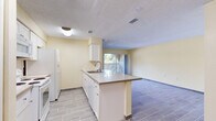 This single-floor, 2-bedroom, 1-bathroom unit offers a practical and comfortable layout designed for efficient everyday living. The open-concept kitchen serves as the heart of the home, featuring white cabinetry, a peninsula island with a light stone-look countertop and bar seating, a double sink, and white appliances including a range, microwave, and refrigerator. Wood-look tile flooring runs throughout the main living areas, lending a clean and cohesive aesthetic. The kitchen flows seamlessly into the living room, which benefits from natural light streaming through a sliding glass door that opens to an outdoor area. Warm yellow-toned walls complement the neutral finishes throughout the space. The two bedrooms are carpeted and offer a quiet, comfortable retreat, with the primary bedroom providing a generous footprint. Four closets distributed throughout the unit ensure abundant storage. The bathroom is well-appointed with a tiled tub-shower combination, a vanity with storage, and wood-look tile flooring consistent with the rest of the home. A hallway connects the private areas of the unit to the main living spaces, completing a thoughtful and functional floor plan.