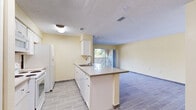 This single-floor, 2-bedroom, 1-bathroom unit offers a practical and comfortable layout designed for efficient everyday living. The open-concept kitchen serves as the heart of the home, featuring white cabinetry, a peninsula island with a light stone-look countertop and bar seating, a double sink, and white appliances including a range, microwave, and refrigerator. Wood-look tile flooring runs throughout the main living areas, lending a clean and cohesive aesthetic. The kitchen flows seamlessly into the living room, which benefits from natural light streaming through a sliding glass door that opens to an outdoor area. Warm yellow-toned walls complement the neutral finishes throughout the space. The two bedrooms are carpeted and offer a quiet, comfortable retreat, with the primary bedroom providing a generous footprint. Four closets distributed throughout the unit ensure abundant storage. The bathroom is well-appointed with a tiled tub-shower combination, a vanity with storage, and wood-look tile flooring consistent with the rest of the home. A hallway connects the private areas of the unit to the main living spaces, completing a thoughtful and functional floor plan.