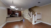 This two-story home offers a thoughtfully designed layout that balances functionality and classic style. The main level showcases gleaming hardwood floors that extend throughout the open-concept living area, creating a warm and inviting atmosphere. The kitchen is a standout feature, equipped with rich dark wood cabinetry, dark stone countertops, a stainless steel refrigerator, and a peninsula that serves as both a prep space and a casual dining area. A pendant light fixture adds a decorative touch above the kitchen, complementing the recessed lighting throughout. Crown molding lines the ceilings, lending the space a refined architectural detail. A prominent staircase with white-painted balusters, sturdy newel posts, and a rich wood handrail serves as the central visual anchor of the main floor. Beneath the staircase, a clever built-in shelving unit provides practical storage while adding a charming design element. The open flow between the kitchen and living areas makes the main level feel spacious and connected. The second floor is accessible via the elegant staircase, offering additional living quarters above. Overall, the home exudes a traditional yet timeless aesthetic with quality finishes and well-utilized space throughout.
