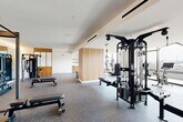 Located at 1070 Bridgeview Way in San Francisco's Mission Bay neighborhood, this modern fitness facility offers a comprehensive and thoughtfully designed workout environment across a single expansive floor. The space is divided into two distinct areas: a well-appointed exercise room and a bright, open studio living area.

The exercise room is generously sized and outfitted with a wide range of professional-grade equipment, including cable machines, a Smith machine, weight benches, dumbbells, kettlebells, rowing machines, and cardio equipment such as treadmills and stationary bikes. Durable rubberized flooring provides safety and functionality throughout. Warm natural wood accent panels and built-in shelving add visual warmth to the otherwise crisp, white interior. Full-length mirrors expand the sense of space, while recessed and linear lighting ensures excellent visibility.

The studio room is a standout feature, showcasing floor-to-ceiling windows and glass doors that flood the light hardwood floors with abundant natural light. A wall of mirrors fitted with elegant wooden ballet barres makes this space ideal for dance, yoga, or barre workouts. The panoramic views of the San Francisco Bay and surrounding cityscape create an inspiring backdrop. A colorful mural adds an artistic touch to the transitional areas, contributing to the facility's dynamic and motivating atmosphere.