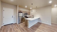 Located at 564–598 16th Ave NE in Watertown, South Dakota, this single-story unit offers a thoughtfully designed layout with a clean, contemporary aesthetic. The open-concept living area features light wood-look luxury vinyl plank flooring, recessed lighting, and a sliding glass door that opens onto a private balcony with neighborhood views, allowing natural light to fill the space.

The kitchen is a standout feature, showcasing a large island with a striking marble-look countertop, a matte black faucet, and pendant lighting overhead. Taupe-toned cabinetry pairs well with stainless steel appliances, including a refrigerator, range, and microwave, creating a functional and stylish cooking environment.

The bedrooms are finished with soft, neutral carpet and feature sliding windows that offer views of the surrounding neighborhood. Baseboard heating units run along the perimeter walls, providing efficient climate control. A walk-in closet with wire shelving systems offers generous storage capacity.

The bathrooms are finished with wood-look LVP flooring, vanities topped with marble-look surfaces, matte black hardware, and well-lit mirrors. One bathroom includes a tub/shower combination. The overall color palette throughout the unit is warm and neutral, contributing to a calm and inviting atmosphere.