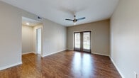 Located at 1511 Mallard Way in Kerrville, Texas, this single-floor unit offers a thoughtfully designed open-concept layout that seamlessly connects the kitchen, dining, and living areas. Rich hardwood-style flooring runs throughout the main living spaces, complementing the warm, neutral-toned walls and clean white trim.

The kitchen is equipped with dark espresso cabinetry, granite countertops, and black appliances, including a refrigerator, electric range, and overhead microwave. A peninsula counter provides additional workspace and serves as a natural divider between the kitchen and the main living area. A dedicated utility closet just off the kitchen houses a stacked washer and dryer for added convenience.

The spacious living room benefits from natural light streaming through double French doors that open to an outdoor view, and a ceiling fan overhead enhances airflow and comfort. The bedroom is carpeted for warmth and comfort, features a ceiling fan, and receives natural light through a large window with blinds.

The bathroom is finished with the same dark cabinetry and granite countertop found in the kitchen, paired with a single-sink vanity, a large mirror, wood-style flooring, and a tiled shower-tub combination. This unit presents a cohesive and functional design throughout.