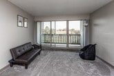 This single-floor residence offers a functional and comfortable layout across several well-defined areas. The living room serves as the heart of the space, featuring plush carpeting, neutral-toned walls, and a textured ceiling. A full-width sliding glass door floods the room with natural light and opens directly onto a private balcony, offering pleasant outdoor views of surrounding greenery and rooftops. A pass-through counter connects the living area to the kitchen, enhancing the open feel between the two spaces.

The galley-style kitchen is efficiently designed, featuring warm oak cabinetry on both sides, ample counter space, and a full suite of appliances including an electric range, refrigerator, and dishwasher. A skylight panel overhead adds brightness to the cooking area, while tile-style flooring provides a durable and easy-to-clean surface.

The bedroom is generously sized with soft carpeting, neutral walls, and a dedicated closet with a hanging rod. A window allows for natural light, and the room connects conveniently to the bathroom. The bathroom includes a single-sink vanity with wood cabinetry, a toilet, and a shower-tub combination. Tile-style flooring completes the space. Overall, the unit presents a clean, practical, and well-lit living environment.