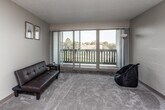 This single-floor residence offers a functional and comfortable layout across several well-defined areas. The living room serves as the heart of the space, featuring plush carpeting, neutral-toned walls, and a textured ceiling. A full-width sliding glass door floods the room with natural light and opens directly onto a private balcony, offering pleasant outdoor views of surrounding greenery and rooftops. A pass-through counter connects the living area to the kitchen, enhancing the open feel between the two spaces.

The galley-style kitchen is efficiently designed, featuring warm oak cabinetry on both sides, ample counter space, and a full suite of appliances including an electric range, refrigerator, and dishwasher. A skylight panel overhead adds brightness to the cooking area, while tile-style flooring provides a durable and easy-to-clean surface.

The bedroom is generously sized with soft carpeting, neutral walls, and a dedicated closet with a hanging rod. A window allows for natural light, and the room connects conveniently to the bathroom. The bathroom includes a single-sink vanity with wood cabinetry, a toilet, and a shower-tub combination. Tile-style flooring completes the space. Overall, the unit presents a clean, practical, and well-lit living environment.