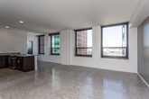 This contemporary urban unit is thoughtfully designed across a single floor, blending modern finishes with an open, functional layout. Polished terrazzo floors run throughout the main living areas, reflecting natural light and lending the space a sleek, refined character.

The open-plan living and dining area is expansive and bright, anchored by large black-framed windows that frame sweeping city views of the surrounding skyline and streetscape. Recessed lighting and clean white walls enhance the airy ambiance throughout.

The kitchen is well-appointed with dark espresso cabinetry, granite countertops, a central island with additional seating, and a full suite of stainless steel appliances including a refrigerator, dishwasher, and microwave. Recessed lighting illuminates the workspace effectively.

Multiple bedrooms offer comfortable accommodations, each featuring large windows with city or urban views, ceiling fans, and generous floor space. The terrazzo flooring continues into these rooms, maintaining a cohesive aesthetic throughout.

The bathroom is generously proportioned, finished with granite countertops atop dark cabinetry, a large walk-in tiled shower with built-in shelving and a bench seat, and accessibility features including grab bars. Bold navy doors provide a striking design contrast throughout the unit.