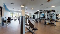 Located at 200 Market St in Montvale, New Jersey, this well-appointed fitness center delivers a comprehensive workout environment across a single thoughtfully designed floor. The space is bathed in natural light, thanks to expansive floor-to-ceiling windows that frame outdoor views and create an open, energizing atmosphere throughout.

The main gym area features warm wood-tone flooring and is outfitted with a broad selection of Life Fitness cardio machines, including treadmills, ellipticals, and steppers, arranged along the windowed perimeter. A dedicated strength training zone houses a full rack of dumbbells, adjustable benches, cable machines, and multi-functional weight stations, all reflected by full-length wall mirrors that visually expand the space.

A separate, carpeted studio room — enclosed by sleek black-framed glass partition walls — provides a quieter setting for yoga, stretching, or group fitness, and is equipped with stability balls and resistance tools. A ceiling fan overhead keeps the room comfortable during active sessions.

The entrance features sophisticated black-framed glass doors that connect seamlessly to adjacent amenity spaces. Bold motivational wall murals add a vibrant, energetic character to the facility, reinforcing its purpose-driven design. The overall ambiance is modern, clean, and inviting — a premium fitness destination built to inspire and perform.