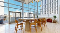 Located in the heart of downtown Phoenix at 44 W Monroe St, this generously sized amenity lounge offers an exceptional blend of modern design and urban sophistication. The interior is anchored by soaring floor-to-ceiling glass curtain walls that flood the space with abundant natural light and frame sweeping views of the Phoenix skyline. Light-toned large-format tile flooring runs throughout, complementing the clean, contemporary aesthetic.

The living area is thoughtfully divided into distinct functional zones. A communal high-top dining table with wood-and-upholstered counter stools sits beneath pendant globe lighting, ideal for social gatherings. Lounge seating areas feature warm caramel leather banquettes, sage green velvet armchairs, and organic-form accent tables, creating inviting spots for relaxed conversation. A dedicated entertainment alcove includes a billiards table, built-in media cabinetry with display shelving, and travertine benches set on richly textured patterned carpet.

The space connects seamlessly to a spacious outdoor terrace, where desert-inspired landscaping with native cacti borders a concrete fire pit with plush seating, an al fresco dining table, and a built-in bar counter with stools — all set against a dramatic downtown backdrop. Warm wall sconces and pendant lighting add an inviting ambiance throughout.