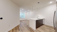 This single-story unit at 5800 Maple Ave in Dallas, Texas offers a thoughtfully designed open-concept layout that maximizes its compact footprint. The combined kitchen and living area forms the heart of the space, anchored by a sleek kitchen island with a white quartz countertop, an undermount sink, and stylish pendant lighting overhead. Dark espresso cabinetry contrasts cleanly with the bright white walls and light wood-look flooring that runs throughout the main living areas. The kitchen is fully equipped with stainless steel appliances, including a side-by-side refrigerator, range, and built-in microwave. Recessed lighting and a ceiling fan keep the living area bright and comfortable, while a window allows natural light to filter in.

The bedroom is a well-proportioned private retreat, finished with plush carpet for added comfort. It connects directly to a dedicated walk-in closet outfitted with built-in shelving and hanging rods, offering practical organization. The full bathroom features a wood-toned vanity with a white countertop, a framed mirror, and clean white walls. The unit's modern, neutral palette and consistent finishes create a cohesive and contemporary ambiance throughout.