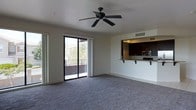 This single-floor space offers an open, airy layout designed for comfortable everyday living. The main living area is finished with plush wall-to-wall carpeting and neutral-toned walls that create a clean, welcoming ambiance. A ceiling fan centered overhead provides both style and functionality, ensuring year-round comfort. A large sliding glass door floods the room with natural light and opens directly onto a private balcony, offering pleasant outdoor views of surrounding greenery — a standout feature of the space.

The kitchen is thoughtfully integrated into the layout via a pass-through design, featuring dark espresso-toned cabinetry, a light granite-style countertop with a breakfast bar overhang ideal for casual dining, and stainless steel appliances including a microwave. Overhead recessed lighting illuminates the kitchen workspace efficiently. A utility sink and ample cabinetry provide practical storage and functionality.

The overall design emphasizes an open flow between the kitchen and living areas, making the space feel expansive and well-connected. With its combination of natural light, outdoor access, and modern kitchen finishes, this space strikes a balance between comfort and practicality.
