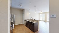 This single-floor residence offers a well-designed open-concept layout that seamlessly connects the kitchen, dining, and living areas. The kitchen is a standout feature, boasting rich dark espresso cabinetry, granite countertops, and a full suite of stainless steel appliances including a refrigerator, microwave, and range. A peninsula with an undermount sink and stylish pendant lighting extends toward the living area, creating a natural gathering space and visual focal point. Hardwood-style flooring flows throughout the main living areas, adding warmth and continuity to the open floor plan. The living room is bathed in natural light, thanks to a set of expansive French doors that open to an outdoor area. A ceiling fan overhead provides additional comfort. The bedroom features plush carpeting and neutral walls, creating a calm and restful environment with ample wall space. The bathroom is finished with light tile flooring, dark vanity cabinetry topped with granite, and a well-lit mirror above the sink, maintaining the consistent design language found throughout the residence. Throughout the space, neutral tones, clean lines, and quality finishes come together to create a cohesive, modern living environment.