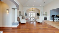 This single-story clubhouse presents an inviting and well-appointed communal space designed with both elegance and functionality in mind. The grand lobby serves as the heart of the space, showcasing soaring vaulted ceilings adorned with a chandelier, decorative archways, and stately white columns that frame the open layout. Rich hardwood flooring flows throughout, complementing the warm, neutral color palette. Upholstered wingback chairs arranged around a central coffee table create a refined seating area, while natural light pours in through French doors and transom windows at the far end.

An adjoining lounge area features high-top bistro tables and chairs positioned near floor-to-ceiling French doors that open to views of an outdoor pool and tropical landscaping, with an arched window above drawing in additional light.

The kitchenette is well-equipped with dark espresso cabinetry, granite countertops, stainless steel appliances including a dishwasher and microwave, a built-in sink, and a wall-mounted television. A dedicated workstation with computers and counter-height seating provides a convenient business center area. A water cooler and additional small appliances complete the practical amenities, making this clubhouse a versatile and comfortable gathering space.