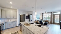 Located at 1300 Front Ave in Columbus, GA, this well-appointed 2-bedroom, 2-bathroom residence offers a thoughtfully designed open-concept layout across a single floor. The kitchen serves as the centerpiece of the living space, showcasing a large granite-topped island with pendant lighting and bar seating, light gray shaker-style cabinetry, white subway tile backsplash, and stainless steel appliances including a refrigerator, range, and built-in microwave. Light hardwood-style flooring flows throughout, connecting the kitchen seamlessly to the spacious living area, which benefits from large windows that fill the room with natural light and a ceiling fan overhead. The primary bedroom is generously sized, featuring plush carpeting and access to a well-appointed en-suite bathroom complete with a dual-sink granite vanity, framed mirrors, and a glass-enclosed shower. A second bedroom and additional full bathroom provide flexible space for guests or a home office. Two closets offer ample storage throughout. A private balcony extends the living space outdoors, offering open views of the surrounding Columbus cityscape and mature tree canopy. The building's brick exterior adds a classic urban character to this modern interior retreat.