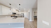 Located at 185 W Kelly St in Metuchen, NJ, this thoughtfully designed 2-bedroom, 1-bathroom residence offers a clean, modern aesthetic across a well-appointed single floor. The open-concept kitchen and living area serves as the heart of the home, showcasing crisp white shaker cabinetry, gleaming quartz countertops, and a full suite of stainless steel appliances including a refrigerator, electric range, and over-the-range microwave. Stylish pendant lighting hangs above the kitchen peninsula, complementing recessed lighting throughout. Light-toned luxury vinyl plank flooring runs seamlessly across the entire space, enhancing the bright, airy feel. The spacious primary bedroom offers generous closet space, while the second bedroom includes its own built-in closet with wire shelving. Both bedrooms feature neutral warm-toned walls and access to the shared full bathroom, which is outfitted with a shaker-style vanity, white quartz countertop, and a tub-shower combination with chrome fixtures. A dedicated in-unit laundry room with a full-size washer and dryer adds everyday convenience. Clean lines, recessed lighting, and a consistent neutral palette give this residence a move-in-ready, contemporary appeal.