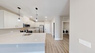 Located at 185 W Kelly St in Metuchen, NJ, this thoughtfully designed 2-bedroom, 1-bathroom residence offers a clean, modern aesthetic across a well-appointed single floor. The open-concept kitchen and living area serves as the heart of the home, showcasing crisp white shaker cabinetry, gleaming quartz countertops, and a full suite of stainless steel appliances including a refrigerator, electric range, and over-the-range microwave. Stylish pendant lighting hangs above the kitchen peninsula, complementing recessed lighting throughout. Light-toned luxury vinyl plank flooring runs seamlessly across the entire space, enhancing the bright, airy feel. The spacious primary bedroom offers generous closet space, while the second bedroom includes its own built-in closet with wire shelving. Both bedrooms feature neutral warm-toned walls and access to the shared full bathroom, which is outfitted with a shaker-style vanity, white quartz countertop, and a tub-shower combination with chrome fixtures. A dedicated in-unit laundry room with a full-size washer and dryer adds everyday convenience. Clean lines, recessed lighting, and a consistent neutral palette give this residence a move-in-ready, contemporary appeal.