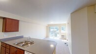 Located at 6950 Birdseye Ave NE in Olympia, Washington, Unit 305 is a thoughtfully designed single-floor residence that combines functional layout with a clean, welcoming aesthetic. The open-concept living and dining area is bathed in natural light, courtesy of sliding glass doors that lead to a private balcony with outdoor views. Soft carpeting underfoot and neutral warm-toned walls contribute to a calm, comfortable atmosphere throughout the living space.

The kitchen is well-appointed with rich, warm-toned cabinetry, a double-basin stainless steel sink, neutral countertops, and a full suite of white appliances including a refrigerator, electric range, microwave, and dishwasher. Durable hardwood-style flooring ties the kitchen together, providing a practical yet attractive contrast to the carpeted living areas.

The bedrooms are generously sized, each featuring plush carpet, large windows that invite natural light and offer views of the surrounding community, and wall-mounted HVAC units for individual climate control.

The bathroom is finished with hardwood-style flooring, a warm wood vanity with ample counter space, chrome fixtures, and a clean, neutral color palette. The overall design of this residence prioritizes bright, open spaces with practical finishes throughout.