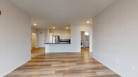 Located at 1447 Water St in Stevens Point, Wisconsin, this single-floor unit presents a clean, modern design with a thoughtfully planned open-concept layout. Light wood-tone flooring flows throughout the main living areas, complementing the bright, neutral palette that defines the space.

The kitchen is well-appointed with white shaker-style cabinetry, dark countertops, and a full suite of stainless steel appliances, including a refrigerator, gas range, and microwave. A peninsula with an integrated sink extends into the living area, creating a natural divide while maintaining an open, connected feel. Recessed lighting overhead keeps the space bright and functional.

The bedrooms feature plush carpeting and large windows with views of the surrounding treeline and neighborhood, allowing natural light to fill each room. One bedroom includes access to a walk-in closet with built-in shelving. The bathroom is designed with accessibility in mind, featuring grab bars, wood-tone vinyl flooring, and a roll-in style shower. A dedicated laundry area houses a full-size Whirlpool front-loading washer and dryer. The overall ambiance is clean, contemporary, and move-in ready.