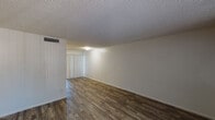 This single-floor unit offers a clean, functional layout designed for comfortable everyday living. Throughout the space, rich wood-style flooring provides a warm, cohesive aesthetic that ties each room together seamlessly.

The open living area is generously proportioned, featuring crisp white walls, a textured ceiling, and a ceiling-mounted HVAC vent for year-round climate control. Vertical blinds on the windows allow for flexible light management while maintaining privacy. The neutral palette creates a bright and airy atmosphere throughout.

The kitchen is efficiently designed, equipped with dark espresso-toned cabinetry that offers ample storage, granite-look countertops, and a full suite of black appliances including a gas range with overhead ventilation hood and a refrigerator. The wood-style flooring continues seamlessly into this space, maintaining visual consistency.

The bedrooms are well-sized, each benefiting from natural light admitted through vertical-blind-covered windows. Built-in wall shelving in the bedroom areas provides convenient storage solutions. The textured ceilings carry throughout, lending a consistent architectural character to the entire unit.

Overall, this space presents a practical and tidy single-level layout with durable finishes, functional storage, and a neutral design scheme well-suited to a variety of living arrangements.