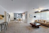This single-floor residence offers a thoughtfully designed open layout that seamlessly connects the living, dining, and entry areas, all finished with plush wall-to-wall carpeting. The living room serves as the centerpiece of the home, highlighted by a white tile-surround fireplace, a ceiling fan, and a bank of large windows that draw in generous natural light and frame views of the surrounding greenery. A dedicated dining area sits adjacent, providing an organized and functional space for everyday living.

The two bedrooms are generously proportioned, each featuring ceiling fans, carpeted floors, and striking deep-blue accent walls that lend a bold, contemporary feel. Both rooms are fitted with ample closet space and are brightened by natural light from large windows with curtains.

The bathrooms are clean and functional, offering wide vanity countertops with under-sink cabinetry, large mirrors, and wood-look flooring. A utility area houses the in-unit washer and dryer alongside additional cabinetry and a full-size refrigerator, adding significant everyday convenience. Neutral gray walls throughout the common areas create a calm, cohesive palette, while accent walls and decor details add personality. The overall ambiance is comfortable, modern, and move-in ready.