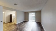 Located at 32122 18th Ave SW in Federal Way, Washington, this single-floor unit offers a thoughtfully laid-out interior finished with dark hardwood-style flooring that runs consistently throughout the living areas, bedrooms, and kitchen. Neutral warm-gray walls and white baseboards create a clean, cohesive aesthetic across the space.

The living area is open and well-proportioned, anchored by a full-width sliding glass door dressed with vertical blinds that admits generous natural light and provides direct outdoor access. The adjacent kitchen is efficiently arranged in a U-shaped configuration, featuring white cabinetry with contemporary hardware, light stone-toned countertops, a stainless steel dishwasher, an electric range, and a window above the sink area that brings in additional natural light.

The bedroom offers a comfortable footprint with a standard window and leads to a dedicated walk-in closet, providing practical storage. The bathroom includes a full tub-shower combination with tile surround, brushed nickel fixtures, and a curved shower rod. Textured ceilings are present throughout. The floor plan, as illustrated by the 3D layout, includes clearly defined rooms connected by a straightforward corridor, offering a functional and livable arrangement.
