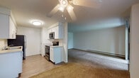 This single-floor residence offers a well-designed layout that balances functionality and comfort throughout its principal spaces. The kitchen is a standout feature, finished with crisp white cabinetry, light countertops, a subway tile backsplash, and a full suite of stainless steel appliances — including a refrigerator, electric range, built-in microwave, and dishwasher. Light wood-look flooring runs underfoot, lending a clean, modern aesthetic to the cooking space.

The kitchen opens directly into a generously sized living and dining area, carpeted in neutral tones and illuminated by a ceiling fan with integrated lighting. A sliding glass door leads to a private balcony, allowing natural light to fill the space and offering pleasant outdoor views of the surrounding neighborhood. An additional window further brightens the room, while baseboard heating ensures year-round comfort.

The bedroom is spacious and carpeted, featuring clean white walls and ample room for furnishings. A hallway connects the bedroom to a full bathroom, which is finished with large-format tile flooring, warm earth-toned tile in the shower surround, a white vanity with under-sink storage, and a well-lit mirror. A louvered closet door in the hallway provides convenient storage access, completing this thoughtfully arranged living space.