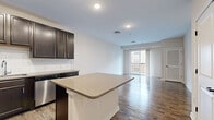 Located at 120 Chubb Ave in Lyndhurst, NJ, this well-appointed one-bedroom, one-bathroom residence offers a thoughtfully designed layout across a single floor. The open-concept kitchen and living area serves as the heart of the space, showcasing rich dark espresso cabinetry, light quartz countertops, a subway tile backsplash, and a full suite of stainless steel appliances. A central kitchen island provides additional prep and seating space, while hardwood-style flooring flows seamlessly throughout the main living areas. Sliding glass doors at the end of the living room invite natural light and open to a private balcony. The bedroom is a comfortable retreat featuring plush wall-to-wall carpeting, a generous window for natural light, and ample closet space. The bathroom is finished with clean white tile flooring, a tub/shower combination, and dark-toned cabinetry with light countertops that mirror the kitchen's aesthetic. A dedicated hallway laundry area accommodates a stacked washer and dryer unit alongside a water heater, adding everyday convenience. Neutral wall tones and recessed lighting throughout the space contribute to a bright, modern, and move-in-ready ambiance.