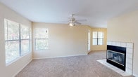 This single-floor residence offers a thoughtfully laid-out living space with a warm, neutral color palette throughout. The open living room is a standout feature, boasting plush wall-to-wall carpeting, a ceiling fan with integrated lighting, and multiple windows that invite abundant natural light and views of lush greenery outdoors. A tile-surround fireplace anchors one end of the room, adding a cozy focal point, while a front entry door with tile flooring provides a clean transition from outside. The kitchen is functional and well-appointed, featuring light wood cabinetry, dark speckled countertops, and wood-style vinyl flooring. It includes a full suite of white appliances — refrigerator, range, built-in microwave, and dishwasher — alongside a double-basin sink. The bedroom is generously sized with soft carpeting and a window fitted with blinds for privacy and light control. The bathroom is finished with wood-style flooring, light wood cabinetry, a dark speckled countertop with an undermount sink, a large mirror, and a full tub-shower combination. Clean lines and consistent finishes throughout give the space a cohesive, move-in-ready feel.