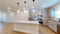 This well-appointed two-story home offers a clean, modern aesthetic throughout, highlighted by light-toned luxury vinyl plank flooring and crisp white walls accented with crown molding. The open-concept main level seamlessly connects the living area to a generously sized kitchen, creating an expansive, airy feel. The kitchen is a standout feature, centering around a large island topped with polished granite countertops and illuminated by a trio of black pendant lights. Shaker-style gray cabinetry lines the walls, complemented by granite counters, a stainless steel range with a wall-mounted hood vent, a French door refrigerator with ice and water dispenser, a built-in microwave, and a dishwasher. A window above the sink draws in natural light. A staircase on the main level leads to the second floor. The bathroom features a granite-topped vanity with undermount sink, gray shaker cabinetry, brushed nickel hardware, large mirrors, and wood-look flooring. Additional rooms are bright and versatile, finished with the same consistent flooring and neutral palette. The attached garage offers a spacious concrete-floored area with an automatic opener, providing ample parking and storage capacity.