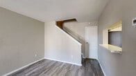 This two-story residence offers a well-organized layout that separates living and sleeping areas across two distinct floors. The main level welcomes you with durable wood-look vinyl plank flooring that flows throughout the open living spaces. A standout feature is the fireplace with a white surround and mantel, anchoring the living room alongside a front entry door and multiple windows dressed with horizontal blinds that allow ample natural light. The adjacent kitchen is efficiently designed with white shaker-style cabinetry, marble-look countertops, and stainless steel appliances including a refrigerator, electric range, and dishwasher. A dedicated dining area sits nearby, illuminated by a ceiling light fixture and a large window overlooking the exterior. A staircase with white railings leads to the upper level, where the bedrooms are finished with plush carpet and feature windows that bring in natural light. The upper level also includes a bathroom appointed with a generous marble-look countertop, dual sinks, and a large wall mirror. Neutral warm-beige tones are consistent throughout the home, creating a cohesive and inviting atmosphere well-suited for comfortable everyday living.