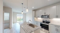 This thoughtfully designed one-bedroom, one-bathroom unit in Round Rock, Texas, offers a clean, modern aesthetic throughout its efficiently organized single-floor layout. The open-concept kitchen and living area serves as the heart of the space, where light hardwood-style flooring, recessed lighting, and stylish pendant lights create a bright and welcoming atmosphere. The kitchen is well-appointed with granite stone countertops, a large island with an undermount sink, white shaker-style cabinetry with matte black hardware, and a full suite of stainless steel appliances including a range, over-the-range microwave, refrigerator, and dishwasher. The living room extends naturally from the kitchen and opens to a private outdoor patio through a sliding glass door, allowing ample natural light and outdoor views. A ceiling fan adds comfort to the space. The bedroom features soft carpeting, a ceiling fan, and a window with natural light. The full bathroom includes granite countertops, a soaking tub, tiled shower surround, and direct access to a dedicated walk-in closet with built-in shelving. A hallway connects all rooms, completing this well-planned and move-in-ready unit.