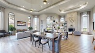 Located at 1600 Eldridge Pkwy in Houston, TX, this thoughtfully designed single-floor space offers a spacious and elegant layout combining a kitchen and living area. The interior is defined by dramatic soaring ceilings with coffered and tray detailing, flooding the space with natural light through a series of tall arched windows that frame lush outdoor greenery. Light wood-tone flooring runs throughout, complementing the neutral, warm color palette of the walls and furnishings.

The living area is generously proportioned, featuring multiple seating zones that create a welcoming and versatile atmosphere. A large floor-to-ceiling window serves as a striking focal point, offering panoramic views of the surrounding landscape. A classic fireplace with a stone surround adds architectural elegance, while curated artwork and open shelving contribute to the space's refined character.

The kitchen area centers around a standout curved bar counter with blue cabinetry and granite countertops, accented by a dark subway tile backsplash and multiple mounted screens above. Bar-height seating adds a social, functional element to this zone. Clean six-panel interior doors and recessed lighting maintain a polished, cohesive aesthetic throughout. Overall, the space exudes a modern yet inviting ambiance, balancing style and comfort.