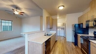 This single-floor residence offers a thoughtfully designed layout with a clean, modern aesthetic throughout. The galley-style kitchen is a standout feature, outfitted with warm wood-toned cabinetry, white quartz countertops, and a full suite of black stainless steel appliances including a refrigerator, electric range, microwave, and dishwasher. Durable wood-look flooring runs the length of the kitchen, which opens to a dedicated in-unit laundry area with side-by-side washer and dryer units — a highly practical convenience. A breakfast bar peninsula connects the kitchen to the adjacent living area, which features a vaulted ceiling with a ceiling fan, adding an airy sense of height and openness. The bedrooms are carpeted and bathed in natural light from large windows; the primary bedroom benefits from its own vaulted ceiling and ceiling fan, lending it a spacious feel. The unit includes two bathrooms: a full bath with a single-basin vanity, tile flooring, and a walk-in shower, and a second bath with a single-basin vanity and toilet. Neutral tones and clean finishes are carried throughout, creating a cohesive and move-in-ready environment well-suited for comfortable everyday living.