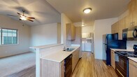 This single-floor residence offers a thoughtfully designed layout with a clean, modern aesthetic throughout. The galley-style kitchen is a standout feature, outfitted with warm wood-toned cabinetry, white quartz countertops, and a full suite of black stainless steel appliances including a refrigerator, electric range, microwave, and dishwasher. Durable wood-look flooring runs the length of the kitchen, which opens to a dedicated in-unit laundry area with side-by-side washer and dryer units — a highly practical convenience. A breakfast bar peninsula connects the kitchen to the adjacent living area, which features a vaulted ceiling with a ceiling fan, adding an airy sense of height and openness. The bedrooms are carpeted and bathed in natural light from large windows; the primary bedroom benefits from its own vaulted ceiling and ceiling fan, lending it a spacious feel. The unit includes two bathrooms: a full bath with a single-basin vanity, tile flooring, and a walk-in shower, and a second bath with a single-basin vanity and toilet. Neutral tones and clean finishes are carried throughout, creating a cohesive and move-in-ready environment well-suited for comfortable everyday living.