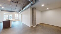 This single-floor unit showcases a compelling blend of industrial and contemporary design elements. The open living area immediately draws attention with its exposed structural concrete columns, large-diameter silver HVAC ductwork running along the ceiling, and polished concrete floors that extend throughout the space. Recessed lighting and a window allowing natural light contribute to a bright, airy atmosphere despite the raw industrial aesthetic.

The kitchen is a standout feature, outfitted with floor-to-ceiling taupe cabinetry, a crisp white quartz countertop, and a full suite of stainless steel appliances including a gas range, over-the-range microwave, and French door refrigerator. A kitchen island with matching countertop provides additional prep and serving space, while the exposed concrete ceiling overhead reinforces the unit's industrial character.

Two bathrooms serve the space. One features a soaking tub and shower combo with classic white subway tile surround, taupe cabinetry with a tall linen tower, an undermount sink with white countertop, and a large frameless mirror. The second bathroom offers a toilet and vanity with matching taupe cabinetry and a large mirror. Both bathrooms continue the polished concrete flooring found throughout the unit, maintaining a cohesive design language from room to room.