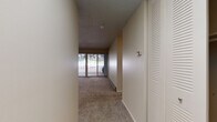 This single-floor residence is thoughtfully laid out to maximize functionality across its living spaces. The entry opens into a carpeted hallway, with a louvered closet door providing convenient storage near the front entrance. A thermostat is positioned along the wall, reflecting practical accessibility throughout the unit.

The living area is generously proportioned, featuring plush carpeting, a textured ceiling, and a baseboard heating system along the perimeter walls. A full wall of sliding glass doors floods the space with natural light and provides direct access to an outdoor patio area, offering views of a distinctive natural rock formation that serves as a scenic backdrop.

The bedroom is a quiet, carpeted room with a window framing the same rocky outdoor landscape, contributing a sense of natural surroundings to the interior.

The galley-style kitchen is well-appointed with rich dark cabinetry, white quartz countertops, warm hardwood flooring, and a full suite of stainless steel appliances including a refrigerator, range, and microwave. A single-basin sink with a modern faucet completes the functional workspace.

The bathroom features a full tub-shower combination with tile surround, complemented by dark vanity cabinetry consistent with the kitchen's design aesthetic.