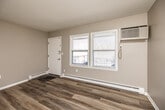 This single-floor unit offers a thoughtfully designed layout that maximizes functionality and comfort. The open living area greets you at the entrance, showcasing durable wood-look vinyl plank flooring, neutral warm-gray walls, and a textured ceiling that runs throughout the space. Natural light filters in through double windows, complemented by a wall-mounted air conditioning unit and baseboard heating for year-round climate control.

The galley-style kitchen is efficiently organized with warm wood cabinetry, dark blue granite-look countertops, a tiled subway backsplash in deep blue-gray tones, and a full suite of black appliances including a refrigerator, electric range, microwave, and dishwasher. A stainless steel sink with a window above adds both practicality and brightness to the cooking space.

A transitional hallway area features a wall-mounted vanity with a dark countertop and mirror, providing a convenient grooming station. The bathroom is neatly appointed with a warm wood vanity, dark granite-style countertop, mirrored medicine cabinet, a chrome towel rack, and a window that brings in additional natural light. Baseboard heating in the bathroom ensures comfort in cooler months. The consistent flooring and cohesive neutral palette throughout create a clean, move-in-ready atmosphere.
