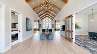 Located at 18300 Marvelous Pl in Cypress, TX, this expansive single-floor community clubhouse is a showcase of modern farmhouse design. The grand entrance foyer greets visitors with soaring vaulted ceilings adorned with exposed wood beams and a striking chandelier, setting an impressive tone throughout. Light wood-look flooring flows seamlessly underfoot, while floor-to-ceiling windows and a dramatic gabled glass facade flood the space with abundant natural light and views of the surrounding community.

The open lounge area is generously proportioned, furnished with tufted benches and curated artwork, creating an inviting social hub. An adjacent dining and kitchen zone features a large communal table with woven rattan seating, pendant lighting, and a sleek wet bar with an eye-catching geometric tile backsplash — ideal for gatherings and events. High-top seating areas with tall windows offer additional casual lounging spots bathed in natural light.

The dedicated fitness center is well-appointed with high ceilings featuring a wood-paneled ceiling and large industrial fan, comprehensive strength and cardio equipment including cable machines, a power rack, treadmills, ellipticals, and a stationary bike, all surrounded by windows overlooking the outdoors. Together, these amenities deliver a refined, functional, and welcoming community experience.