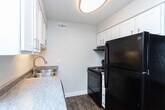 Located at 4450 S Lemans Dr in Millcreek, Utah, this one-bedroom, one-bathroom unit offers a thoughtfully utilized single-floor layout. Wood-look flooring flows consistently throughout, lending a warm and cohesive aesthetic to every room.

The living room is bright and welcoming, featuring a large window with blinds that allows natural light to fill the space, complemented by a wall-mounted HVAC unit and a ceiling fan for year-round comfort. The entry door opens directly into this area, creating an accessible and open feel.

The kitchen is efficiently designed in a galley-style configuration, featuring crisp white cabinetry with modern hardware, gray laminate countertops, a stainless steel sink, and black appliances including a refrigerator, range, and dishwasher. A ceiling-mounted light fixture provides ample illumination.

The bedroom is a comfortable, well-proportioned room with a large window offering outdoor views and abundant natural light. Clean white walls and the same wood-look flooring maintain the unit's consistent design language.

The bathroom is finished with a white vanity featuring a stone-look countertop, a tub-shower combination with a curved curtain rod, and a narrow window for ventilation. A connecting hallway links the rooms with a clean, functional layout throughout.
