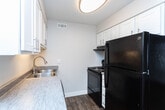 Located at 4450 S Lemans Dr in Millcreek, Utah, this one-bedroom, one-bathroom unit offers a thoughtfully utilized single-floor layout. Wood-look flooring flows consistently throughout, lending a warm and cohesive aesthetic to every room.

The living room is bright and welcoming, featuring a large window with blinds that allows natural light to fill the space, complemented by a wall-mounted HVAC unit and a ceiling fan for year-round comfort. The entry door opens directly into this area, creating an accessible and open feel.

The kitchen is efficiently designed in a galley-style configuration, featuring crisp white cabinetry with modern hardware, gray laminate countertops, a stainless steel sink, and black appliances including a refrigerator, range, and dishwasher. A ceiling-mounted light fixture provides ample illumination.

The bedroom is a comfortable, well-proportioned room with a large window offering outdoor views and abundant natural light. Clean white walls and the same wood-look flooring maintain the unit's consistent design language.

The bathroom is finished with a white vanity featuring a stone-look countertop, a tub-shower combination with a curved curtain rod, and a narrow window for ventilation. A connecting hallway links the rooms with a clean, functional layout throughout.