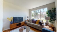 Located at 6924 NW 159th Ave in Portland, Oregon, this single-floor residence offers a well-organized layout that balances open communal spaces with comfortable private quarters. The living room serves as the heart of the home, featuring warm hardwood flooring, a textured ceiling, and a generously sized picture window that floods the space with natural light and frames views of the surrounding neighborhood's mature trees and greenery. The open-concept design connects the living area seamlessly to the kitchen, which is outfitted with warm wood cabinetry, light stone countertops, a full suite of stainless steel appliances—including a refrigerator, range, microwave, and dishwasher—and a pendant light above the sink area. Two bedrooms provide restful retreats, each carpeted and featuring windows that bring in additional natural light; one bedroom includes a walk-in closet. The two bathrooms are finished consistently with wood-toned vanity cabinetry, white countertops, large mirrors with overhead lighting, and tiled flooring. Throughout the residence, a cohesive neutral palette punctuated by warm wood tones creates a calm, contemporary ambiance well-suited to everyday living.