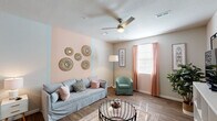 This single-floor residence offers a warm and inviting atmosphere through a cohesive blend of soft color palettes, wood-look flooring, and contemporary finishes throughout. The living room serves as the heart of the home, highlighted by a blush-toned accent wall adorned with decorative woven mirrors, wood-look flooring, and a ceiling fan overhead. Natural light filters in through a window dressed with coral curtains, creating a bright and airy feel. An adjacent area provides additional living space with neutral tones and ample room for entertainment or relaxation. The dining area features a pendant light fixture above a round wooden table, offering an intimate setting for meals. The kitchen is well-equipped with granite-style countertops, dark cabinetry, stainless steel appliances, and light wood-look flooring, combining functionality with modern style. The primary bedroom is carpeted and features a bold navy horizontal accent wall, a ceiling fan, and a window with patterned curtains. A second bedroom offers a softer aesthetic with a blush accent wall, carpeted floors, and a ceiling fan. A generously sized walk-in closet with wire shelving provides substantial storage. The bathroom includes a tub-shower combination, wood-look flooring, and a vanity with granite-style countertops, completing this well-rounded and comfortable home.