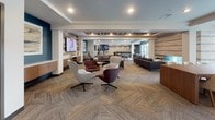 The Club Room is a thoughtfully designed communal space that blends comfort, style, and functionality across a single expansive floor. The open layout flows seamlessly between distinct activity zones, each curated to encourage both relaxation and social engagement.

The fully equipped kitchen is a standout feature, showcasing warm wood cabinetry, a quartz countertop, and a striking hexagonal tile backsplash that adds a bold geometric accent. Open floating shelves, a gas cooktop with a stainless steel range hood, double wall ovens, and a large central island with seating for multiple guests make this an ideal space for gatherings and entertaining.

The lounge area is generously sized, featuring patterned herringbone carpeting, bold accent walls in deep blue, and a reclaimed wood ceiling inset that adds warmth and texture. A large wall-mounted television anchors one end, surrounded by a mix of modern swivel chairs, a leather sofa, and built-in cabinetry. Adjacent seating arrangements and a long communal table provide flexible options for both casual socializing and group meetings.

A game area with a billiards table offers additional recreational appeal, while a dining nook with a round white table and upholstered chairs sits beside expansive floor-to-ceiling sliding glass doors. These doors open directly onto an outdoor terrace furnished with seating, providing abundant natural light and a strong indoor-outdoor connection.