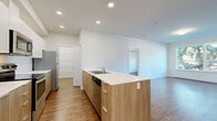 Located at 1085 Goldstream Ave in Victoria, BC, this well-designed 2-bedroom, 2-bathroom unit offers a clean, modern aesthetic throughout. Wood-look laminate flooring flows seamlessly across the entire space, complementing the crisp white walls and creating a warm, cohesive feel.

The open-concept kitchen is a standout feature, equipped with stainless steel appliances including a range, microwave, and refrigerator. Contemporary two-tone cabinetry — white uppers paired with natural wood-finish lowers — lines both sides of the galley-style layout, offering generous storage and white quartz countertops. A peninsula counter with matching cabinetry connects the kitchen to the living area, ideal for casual dining or entertaining.

Both bedrooms are bright and comfortable, with large windows that invite natural light and frame views of mature trees and surrounding greenery. Each bedroom includes a dedicated closet with bi-fold doors, providing practical storage. The primary bedroom also features access to a private balcony.

The two bathrooms are finished in a consistent modern style, featuring wood-tone vanities with white countertops and large mirrors. One bathroom includes a shower-tub combo, while the other offers a walk-in shower. Recessed lighting and baseboard heating are present throughout, completing this well-appointed and move-in-ready home.