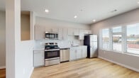 This well-appointed single-floor unit offers a clean, modern aesthetic defined by an open-concept layout and consistent use of light-toned luxury vinyl plank flooring throughout. The kitchen is a functional centerpiece of the space, outfitted with gray shaker-style cabinetry, light stone-patterned countertops, and a full suite of stainless steel appliances including a gas range, built-in microwave, dishwasher, and refrigerator. A pass-through opening connects the kitchen to the adjacent living and dining areas, enhancing the sense of openness and flow. The living area benefits from natural light streaming in through windows fitted with horizontal blinds, and a ceiling fan adds both comfort and visual interest overhead. Recessed lighting throughout ensures consistent, modern illumination across all spaces. A corridor leads to the bathroom, which features a full tub-shower combination with clean white surrounds and chrome fixtures, all continuing the unit's crisp, neutral palette. A dedicated in-unit laundry closet provides added convenience. The layout is efficiently designed, making excellent use of the available space while maintaining a comfortable, airy atmosphere suited to everyday living.