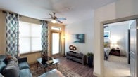 This single-story residence is designed with a cohesive contemporary aesthetic carried consistently throughout its rooms. The living area serves as the heart of the home, featuring wood-style flooring, a ceiling fan, and multiple windows dressed with patterned curtains that allow ample natural light. A glass coffee table and teal sectional sofa anchor the space, which flows directly into the kitchen and dining areas.

The kitchen is well-equipped with dark espresso cabinetry, granite countertops, stainless steel appliances including a range, built-in microwave, and French door refrigerator, alongside a double-basin sink and track lighting overhead. Adjacent to the kitchen, the dining area accommodates a four-seat table beneath matching track lighting, complemented by a decorative mirror and louvered utility closet door.

Both bedrooms offer carpet flooring, ceiling fans, large windows with blinds and drapes, and comfortable proportions. The bathroom features dark cabinetry paired with granite countertops, a large framed mirror, walk-in glass shower, and wood-style flooring. A dedicated laundry room houses a full-size washer and dryer with overhead wire shelving for added storage.