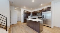 This three-story home showcases a modern design aesthetic with consistent, quality finishes across all levels. The kitchen serves as a central highlight, featuring rich dark espresso cabinetry, a grey tile backsplash, and a full suite of stainless steel appliances including a range, built-in microwave, and French door refrigerator with ice dispenser. A sizeable central island with a white countertop and undermount sink provides additional workspace and casual seating. Light hardwood-style flooring runs throughout the main living areas, creating a warm, cohesive look.

The bathrooms reflect the same clean, contemporary style. A full bathroom includes a glass-door walk-in shower with white surround and built-in shelving, while a separate powder room features a pedestal sink, mirror, and efficient layout. A dedicated laundry room with side-by-side washer and dryer, overhead shelving, and hardwood-style flooring adds practical convenience.

Bedrooms are carpeted for comfort and include windows with blinds, allowing for natural light. One bedroom features a ceiling fan with integrated lighting. Additional flexible rooms with hardwood-style flooring offer versatile use as offices or flex spaces. Recessed lighting throughout maintains a bright, polished ambiance.
