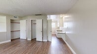 Located at 3075 Park Ave in Merced, California, this efficiently designed single-floor unit offers a thoughtful layout that maximizes every square foot. The combined kitchen and living area serves as the heart of the space, with the living room featuring warm hardwood-style flooring, neutral gray walls, a textured ceiling, and two windows that invite natural light and views of surrounding greenery. A rich, dark wood entry door adds a striking contrast to the light interior palette. The kitchen is well-appointed with white cabinetry, granite-style countertops, a stainless steel double sink, and white appliances including a refrigerator and range. A window above the counter brightens the cooking area. The sleeping area provides generous built-in shelving and closet space, offering practical storage solutions within a compact footprint. The bathroom features a white vanity with granite-style countertops, a bathtub with shower, and consistent hardwood-style flooring that ties the space together. Ceiling-mounted HVAC vents are present throughout, ensuring year-round comfort. The clean, neutral finishes and functional design make this a practical and comfortable space in Merced's residential landscape.