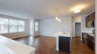 This single-floor residence features a thoughtfully designed open-concept layout that seamlessly connects the kitchen, dining, and living areas. Rich hardwood-style flooring flows throughout the main living spaces, complementing the neutral wall tones and creating a warm, cohesive aesthetic.

The kitchen is a standout feature, centered around a substantial island with a white countertop and integrated sink, illuminated by a trio of pendant lights. Dark espresso cabinetry extends to the ceiling, providing generous storage, while a full suite of stainless steel appliances — including a refrigerator, range, and built-in microwave — adds a polished, modern finish. The adjacent living area benefits from multiple windows that invite natural light and offer views of the surrounding neighborhood.

The bedrooms are carpeted for comfort, with one featuring a spacious walk-in closet and direct access to a private en-suite bathroom equipped with a glass-enclosed shower. A second bathroom includes a full soaking tub and shower combination. Both bathrooms share a consistent design language with dark wood vanities, white countertops, and well-lit vanity mirrors. The overall ambiance is clean, contemporary, and move-in ready.
